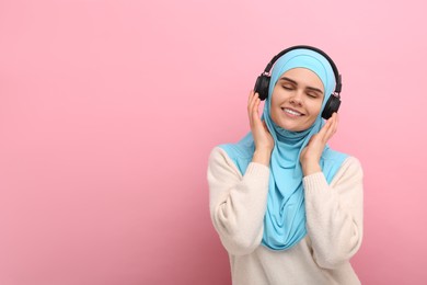 Photo of Muslim woman in hijab and headphones listening to music on pink background, space for text