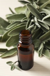 Bottle of essential sage oil and leaves on white wooden table
