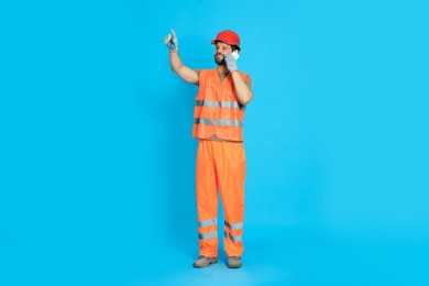Man in reflective uniform talking on smartphone against light blue background