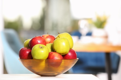 Photo of Bowl with different sweet apples on table in room, space for text