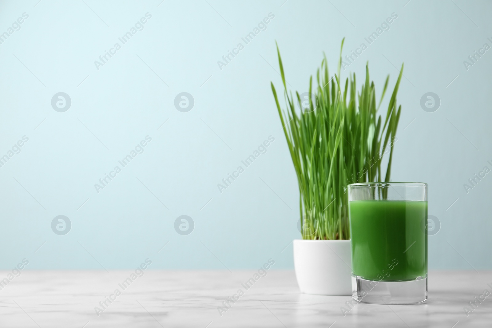 Photo of Glass of juice and sprouted wheat grass on table. Space for text