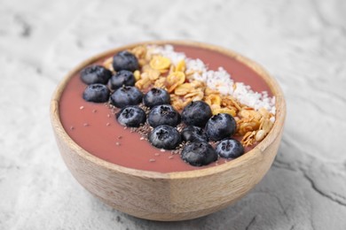 Photo of Bowl of delicious fruit smoothie with fresh blueberries, granola and coconut flakes on white textured table, closeup