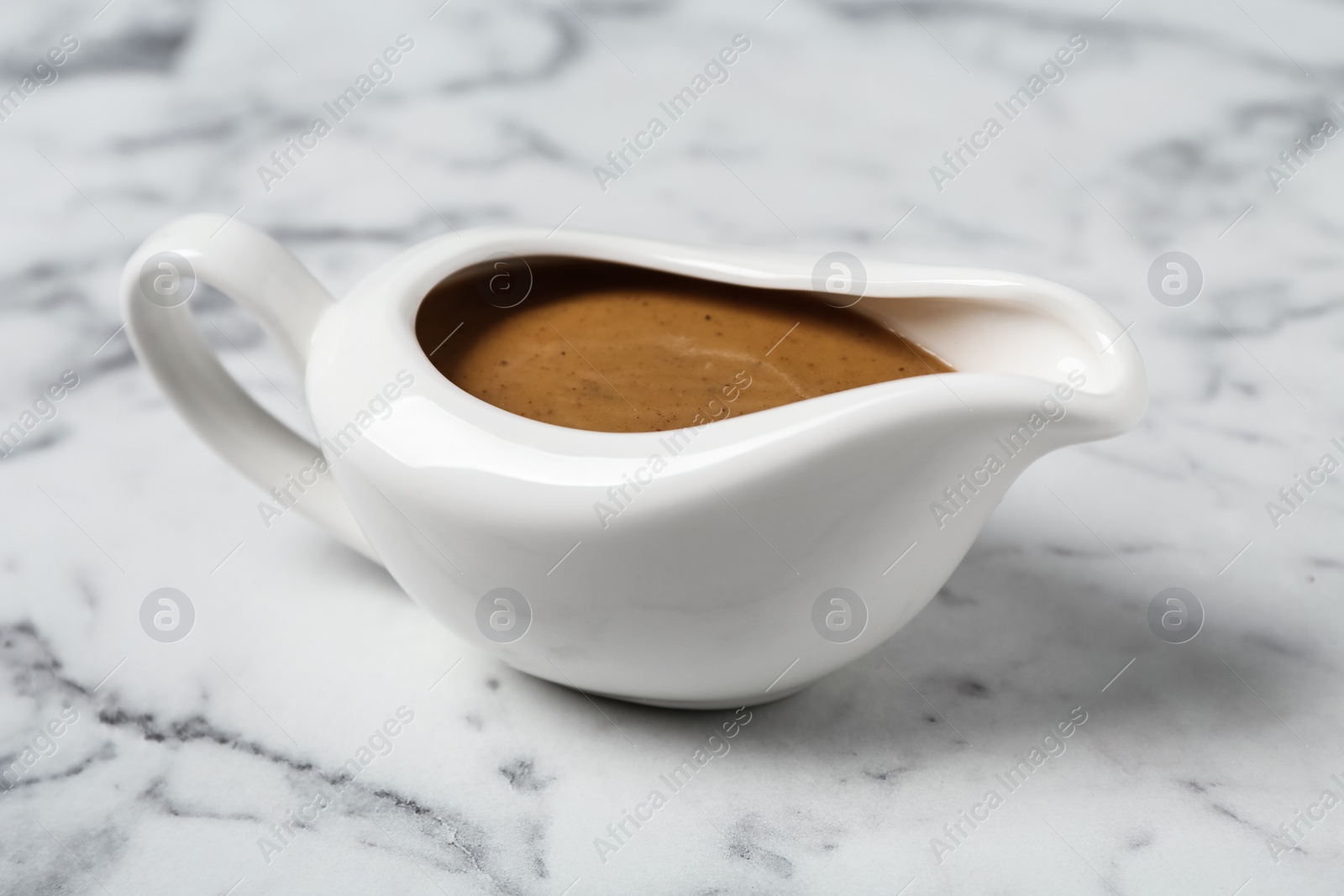 Photo of Delicious turkey gravy in sauce boat on white marble table