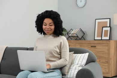 Happy young woman using laptop on sofa indoors