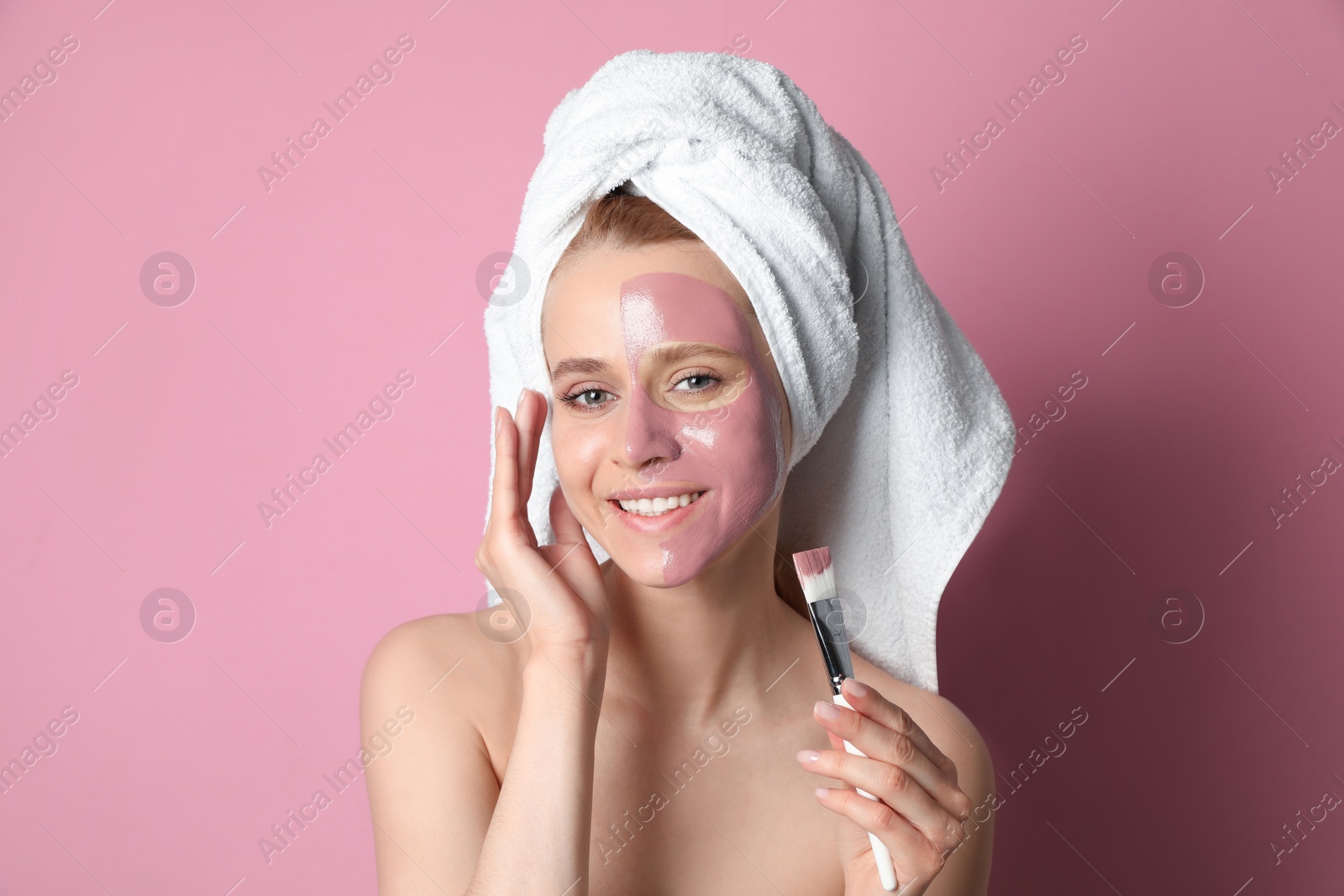 Photo of Young woman applying pomegranate face mask on pink background