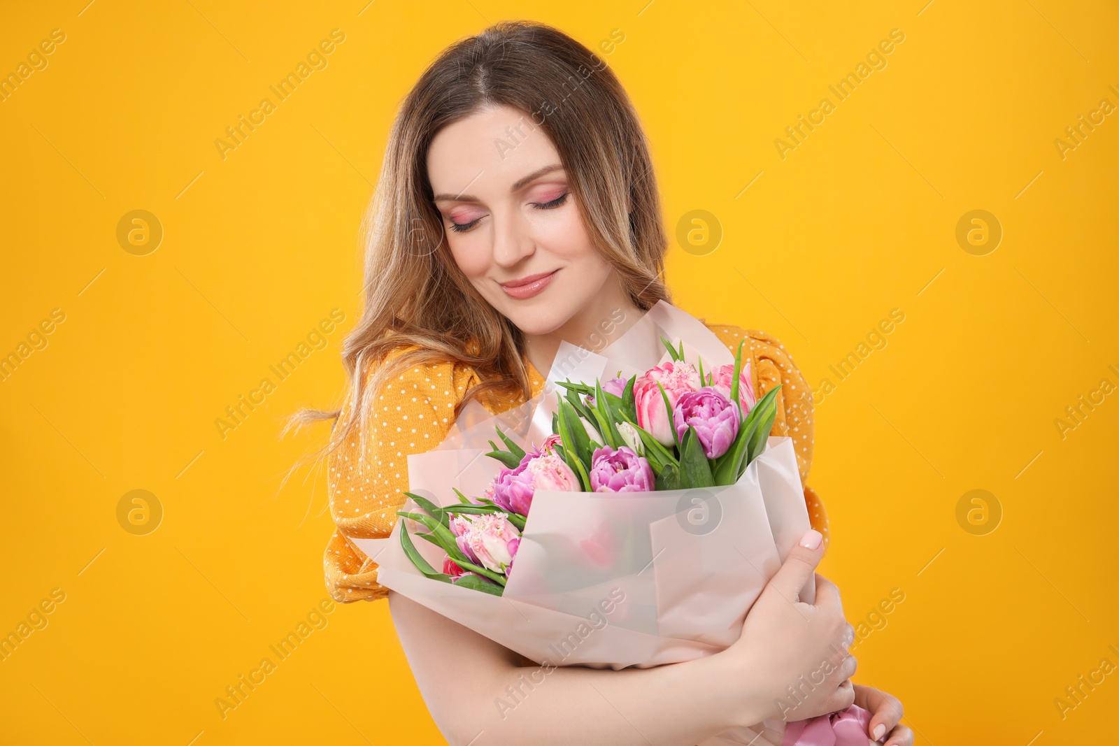 Photo of Happy young woman with bouquet of beautiful tulips on yellow background