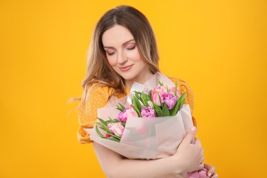 Happy young woman with bouquet of beautiful tulips on yellow background