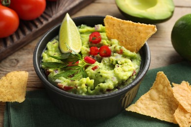 Photo of Delicious guacamole served with nachos chips on wooden table, closeup