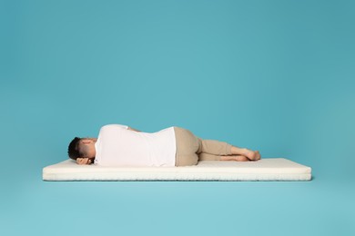 Man sleeping on soft mattress against light blue background, back view
