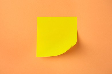 Blank paper note on pale orange background, top view