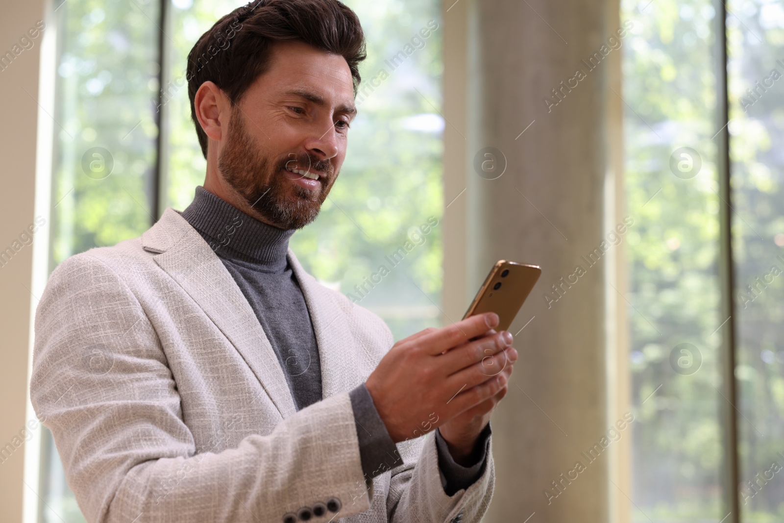 Photo of Positive handsome man using his smartphone indoors