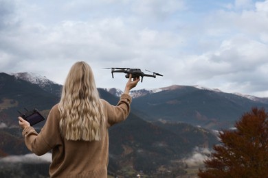 Photo of Young woman with modern drone in mountains, back view. Space for text