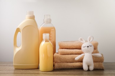 Photo of Bottles of laundry detergents, stacked fresh towels and knitted toy rabbit on table against white background