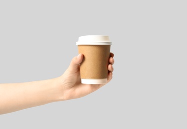 Woman holding takeaway paper coffee cup on light grey background, closeup