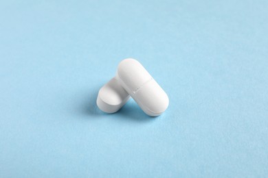 Photo of Two white pills on light blue background, closeup