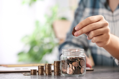 Woman putting money into glass jar at table, closeup