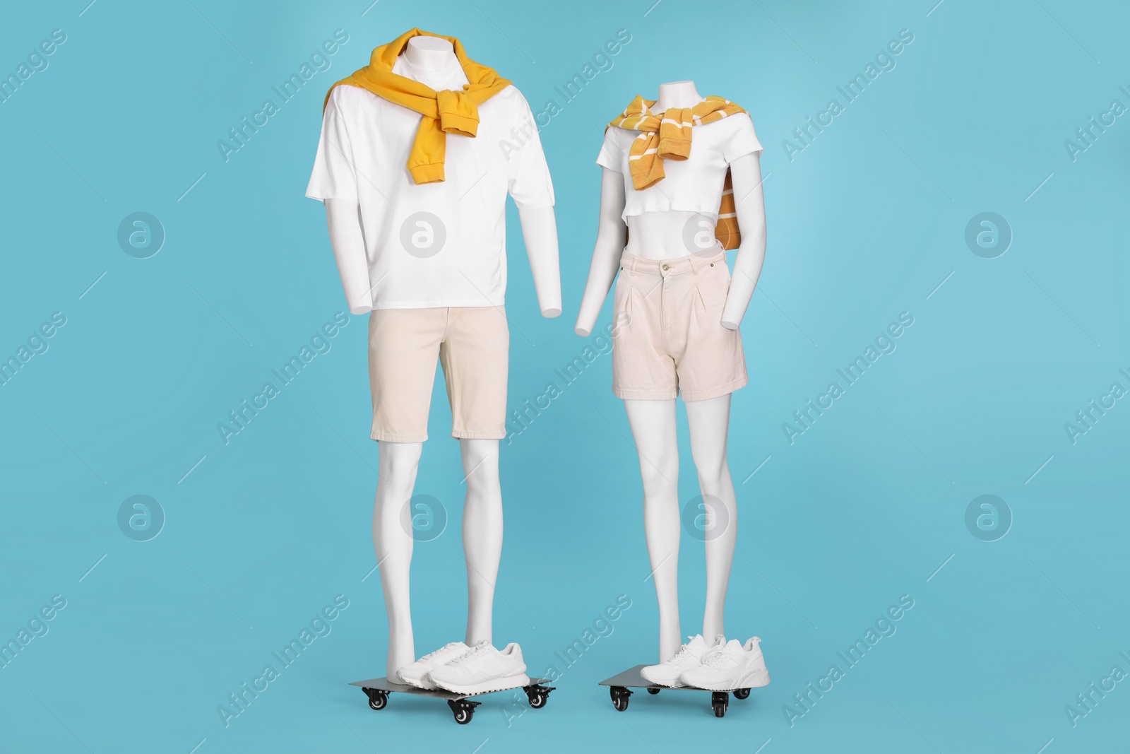 Photo of Female and male mannequins with sneakers dressed in white t-shirts, stylish shorts and orange sweaters on light blue background