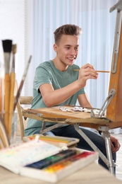 Photo of Teenage boy painting on easel in workshop. Hobby club