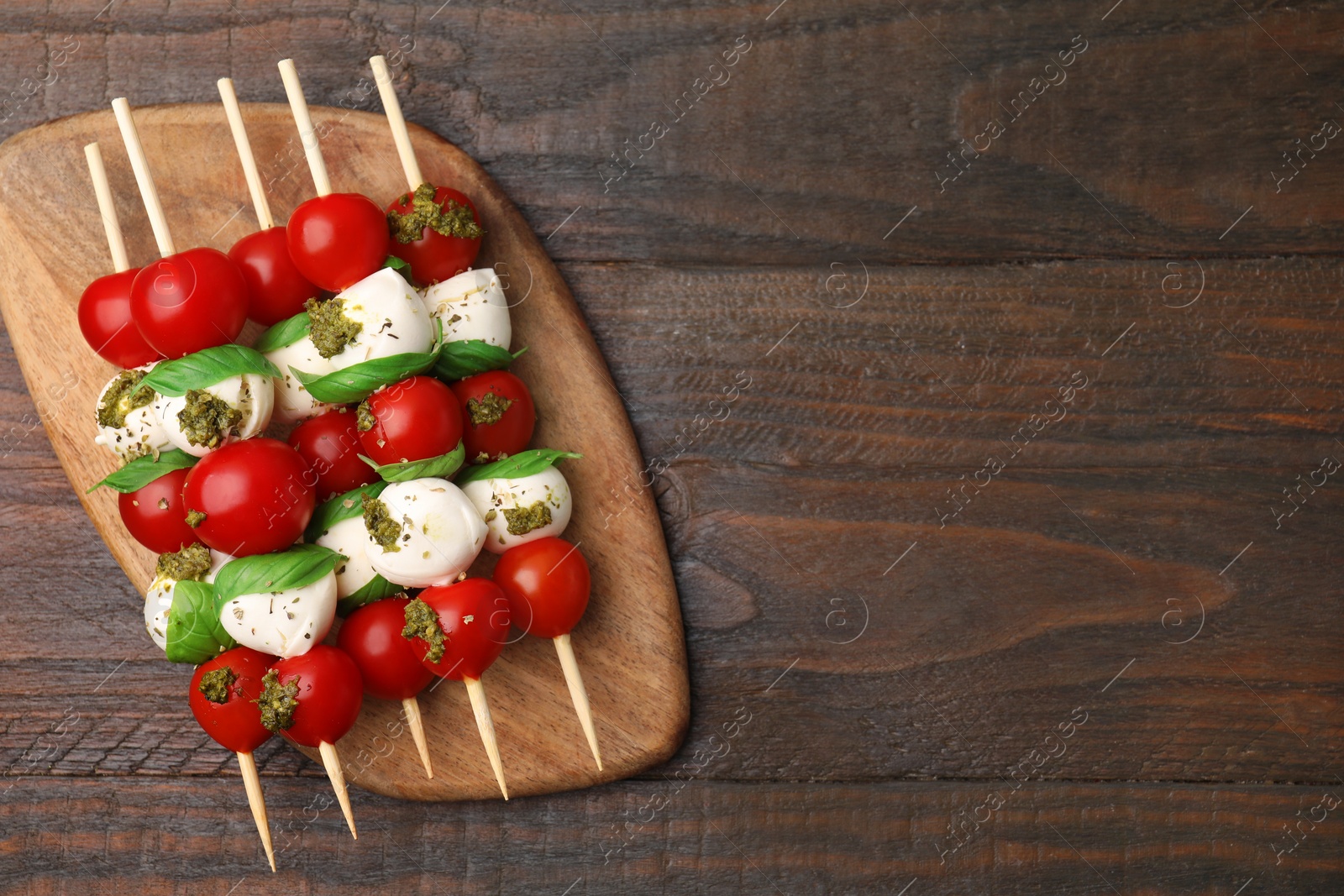 Photo of Caprese skewers with tomatoes, mozzarella balls, basil and pesto sauce on wooden table, top view. Space for text