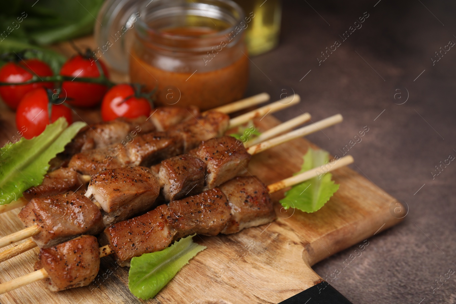 Photo of Tasty cooked marinated meat served with sauce and tomatoes on table, closeup. Space for text