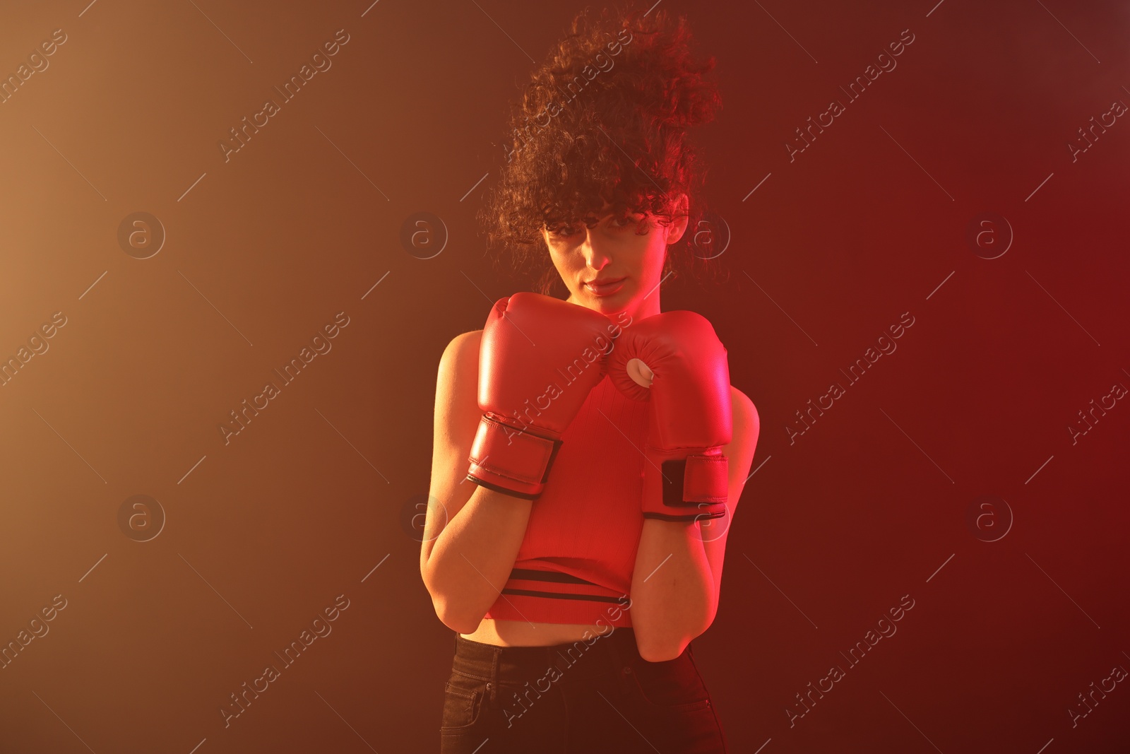 Photo of Beautiful young woman with boxing gloves on color background in neon lights and smoke
