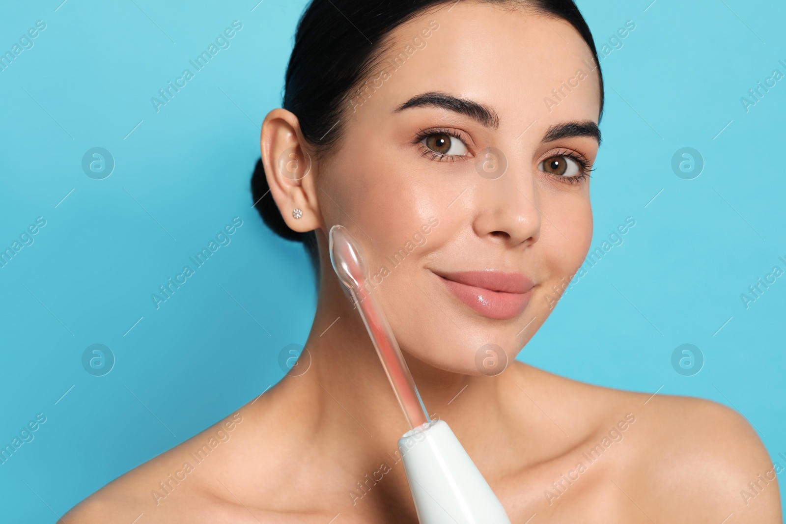 Photo of Woman using high frequency darsonval device on light blue background