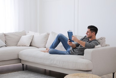 Man with book lying on comfortable sofa in living room