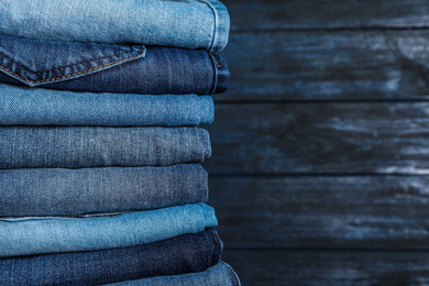 Photo of Stack of different jeans on wooden background, closeup. Space for text