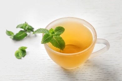 Photo of Cup with hot aromatic mint tea and fresh leaves on table