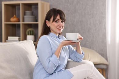 Photo of Beautiful young housewife with cup of drink on sofa at home