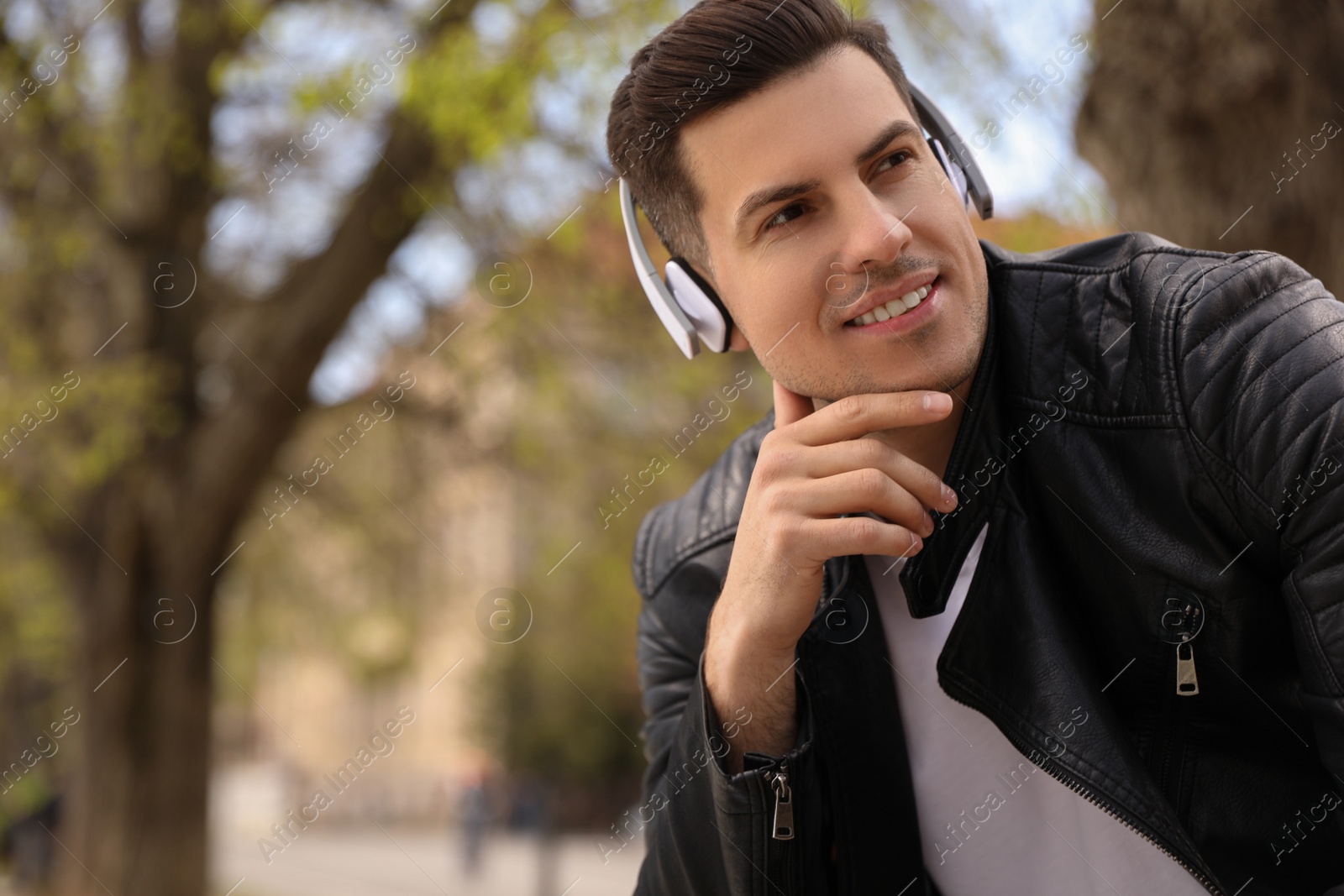 Photo of Handsome man with headphones listening to music outdoors, space for text