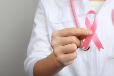 Photo of Doctor holding pink ribbon on grey background, closeup with space for text. Breast cancer awareness