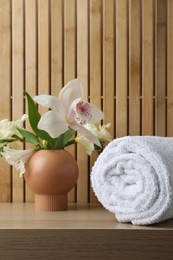 Rolled terry towel and beautiful flowers on wooden table