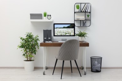 Photo of Cozy workspace with computer on wooden desk and comfortable chair at home