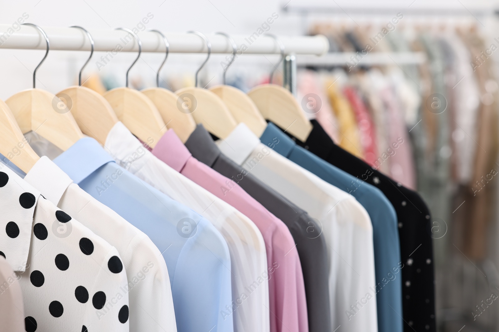 Photo of Dry-cleaning service. Many different clothes hanging on rack indoors, closeup