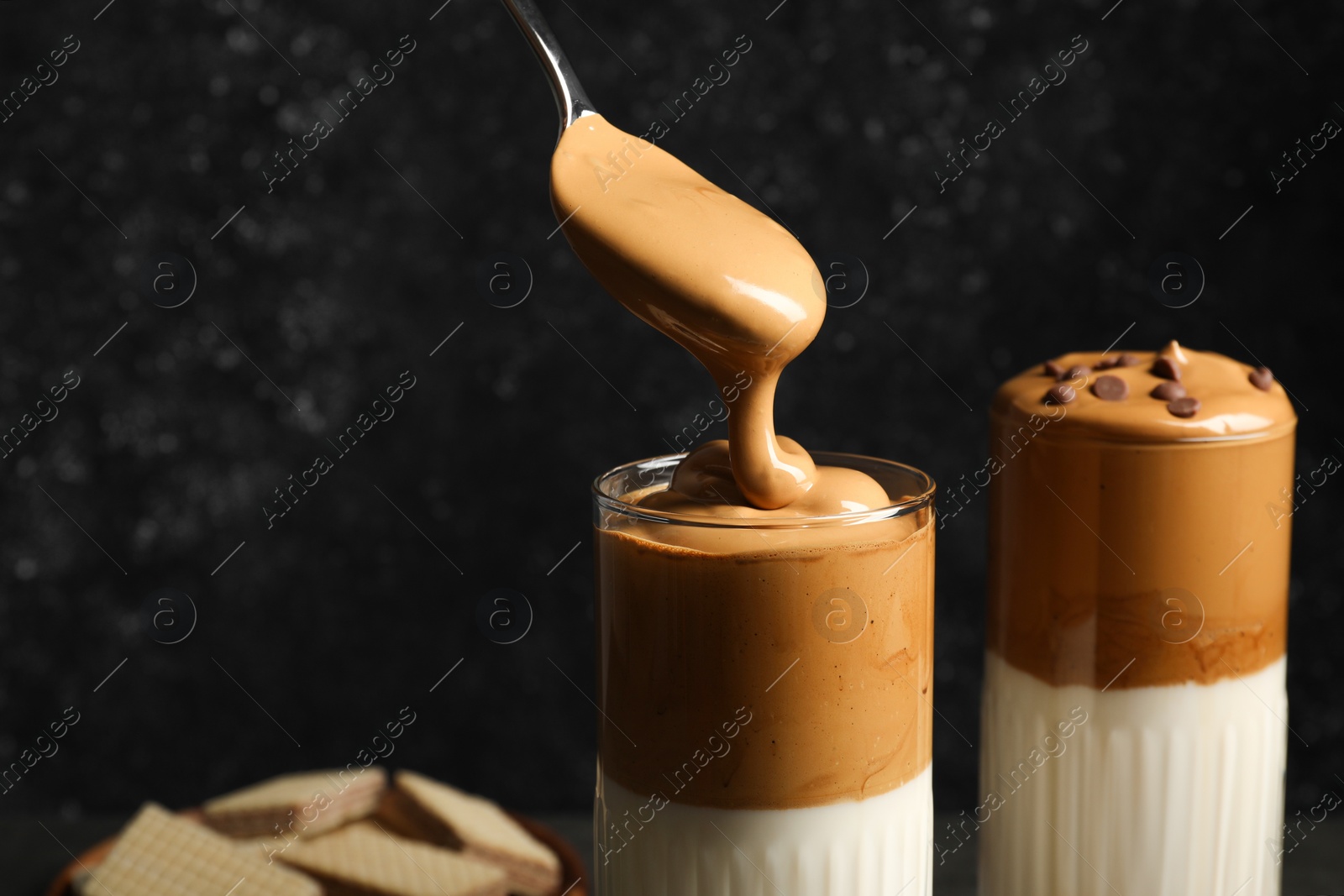 Photo of Pouring cream for dalgona coffee into glass on dark background, closeup