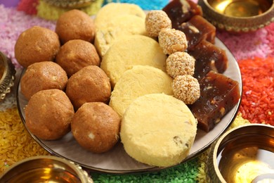 Diwali celebration. Tasty Indian sweets, diya lamps and colorful rangoli on table, closeup