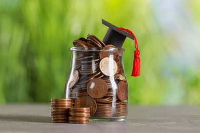 Photo of Scholarship concept. Graduation cap and jar with coins on grey table against blurred background