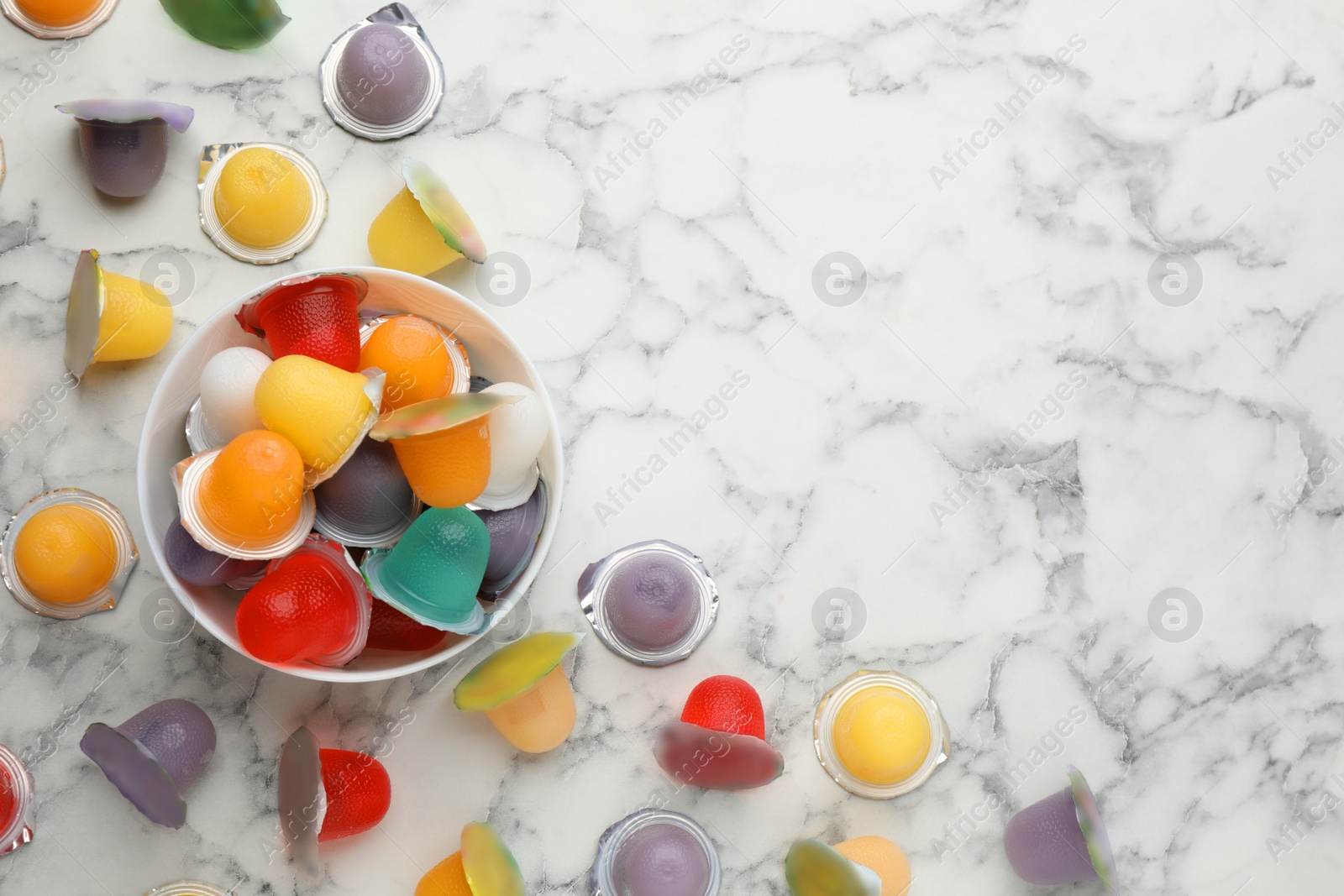 Photo of Bowl with tasty bright jelly cups on white marble table, flat lay. Space for text