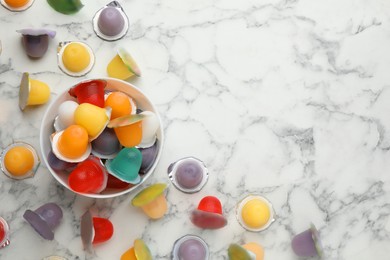 Photo of Bowl with tasty bright jelly cups on white marble table, flat lay. Space for text