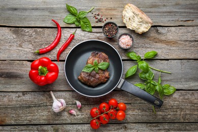 Frying pan with tasty cooked steak and fresh vegetables on wooden table, flat lay