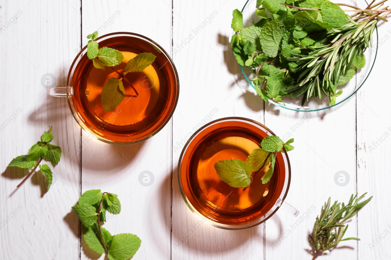 Photo of Cups of aromatic herbal tea with mint and rosemary on white wooden table, flat lay