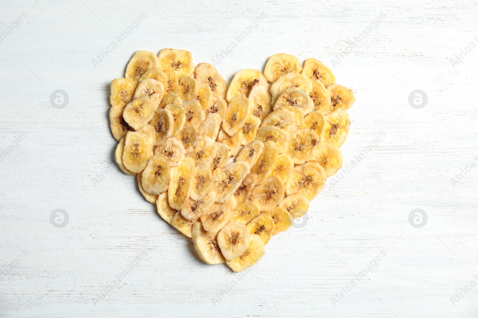 Photo of Heart shape made of sweet banana slices on wooden table, top view. Dried fruit as healthy snack