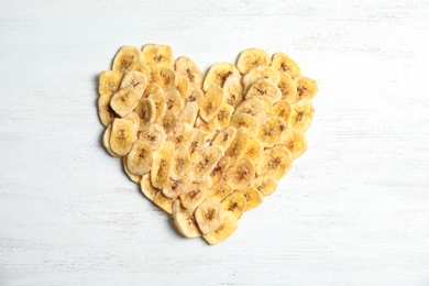 Heart shape made of sweet banana slices on wooden table, top view. Dried fruit as healthy snack