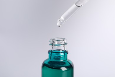 Photo of Dripping cosmetic serum from pipette into bottle on light grey background