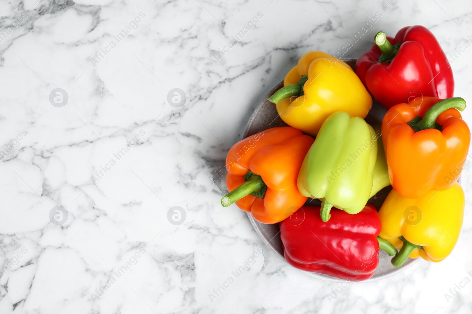 Photo of Plate with ripe bell peppers on marble table, top view. Space for text