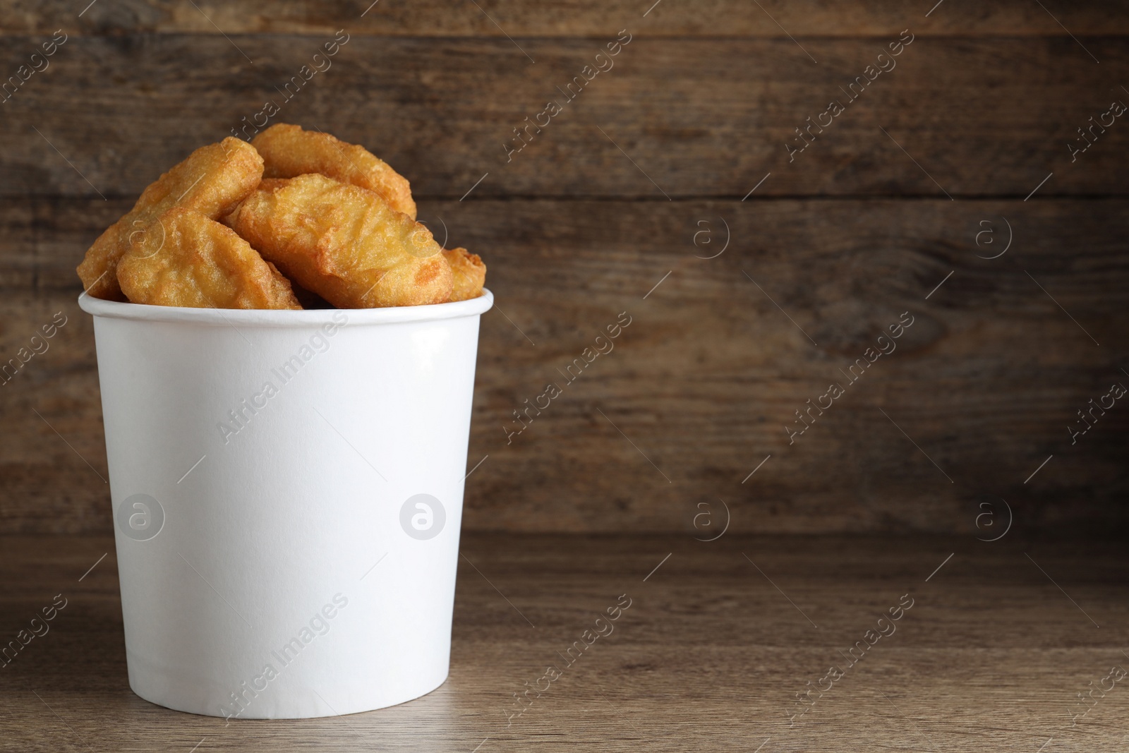 Photo of Bucket with tasty chicken nuggets on wooden table. Space for text