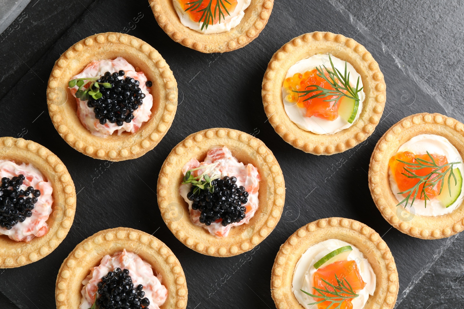 Photo of Delicious canapes with salmon and caviar on black textured table, flat lay