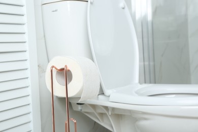 Holder with paper roll near toilet bowl in bathroom