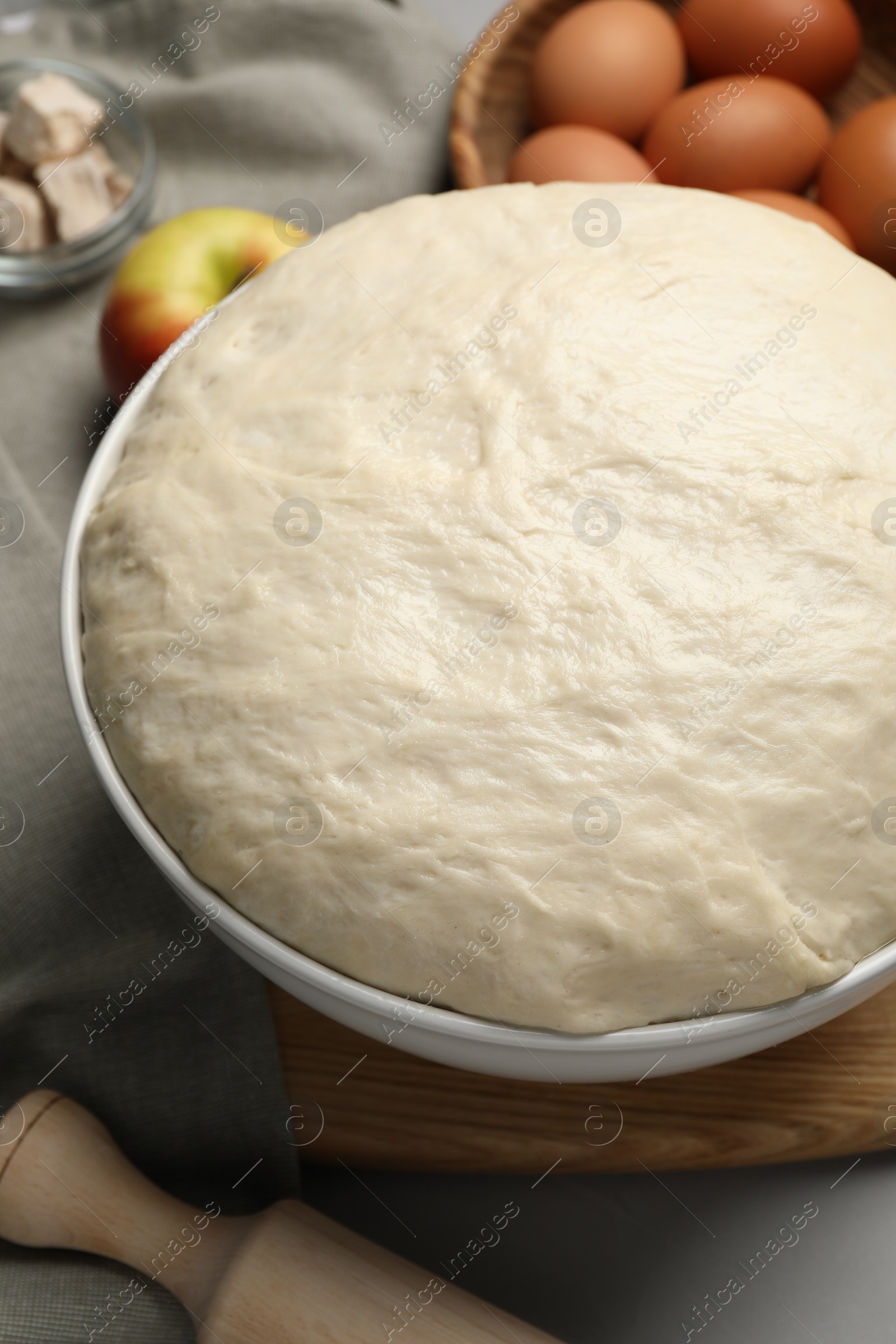 Photo of Fresh dough, rolling pin and ingredients on grey table, closeup. Cooking yeast cake